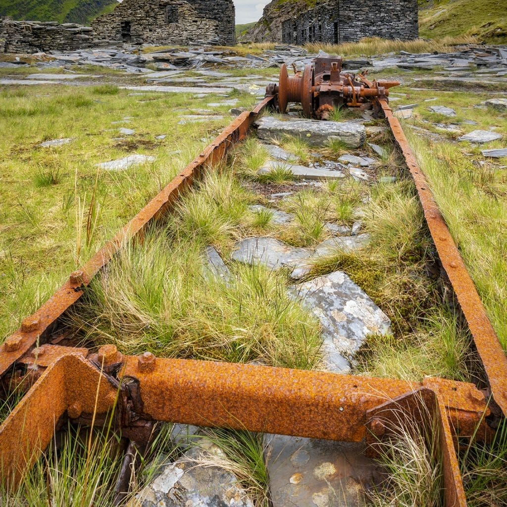 Walking with Your Camera Photographic Workshop from Welshot and Team Leader Helen Iles - Photo is of old disused railway machinery with the ruins of the quarry-mans cottages in the background high in the mountains of the Snowdonia National Park