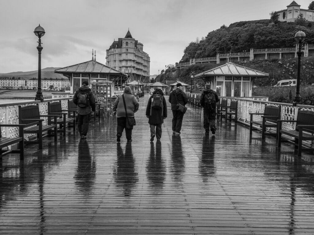 Black and White Photo of five photographers from the Welshot Photographic Academy walking along the Llandudno pier in the wet and rain after a photo workshop