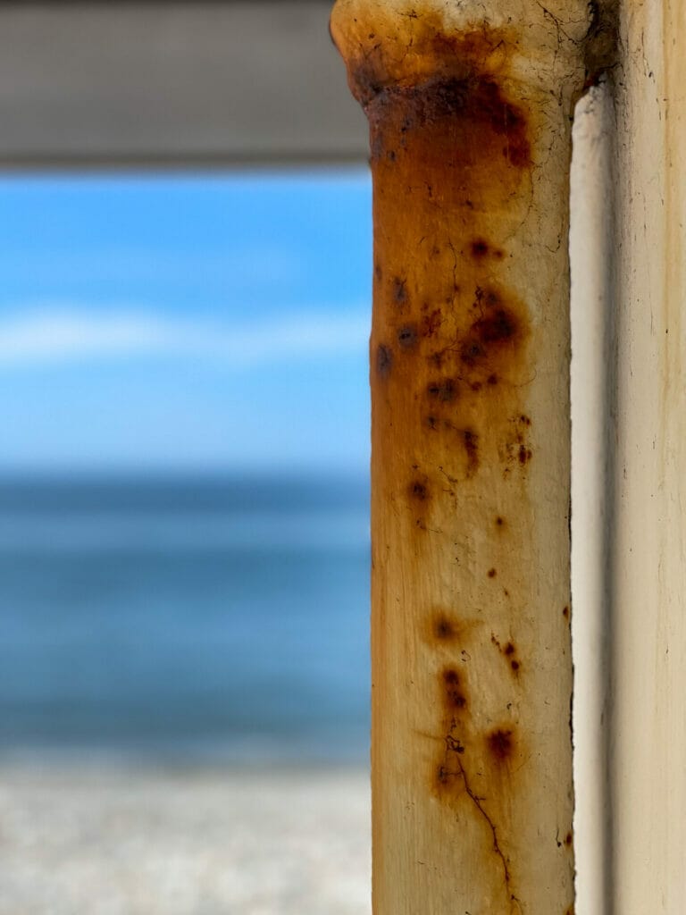 A photo looking through a window of a shelter on the Llandudno prom in North Wales looking toward the blue sea and sky