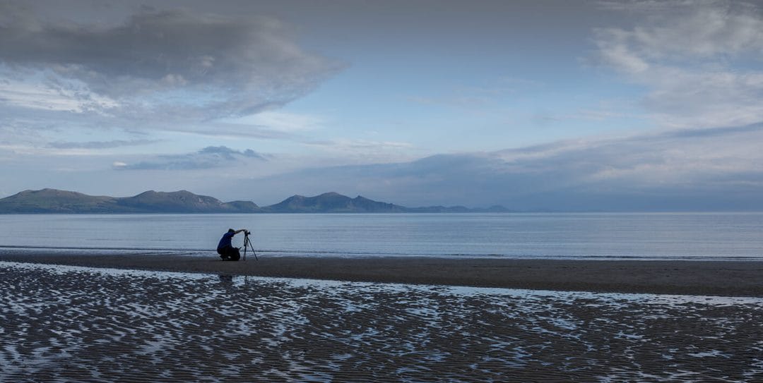 Photo of a lone photographer with a tripod taking a seascape and long exposure on Newborough beach on Anglesey