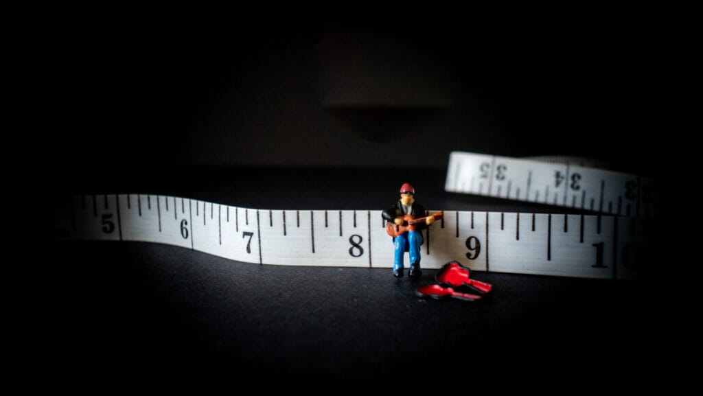 Creative photo showing a miniature model person playing a guitar on a tape measure. 