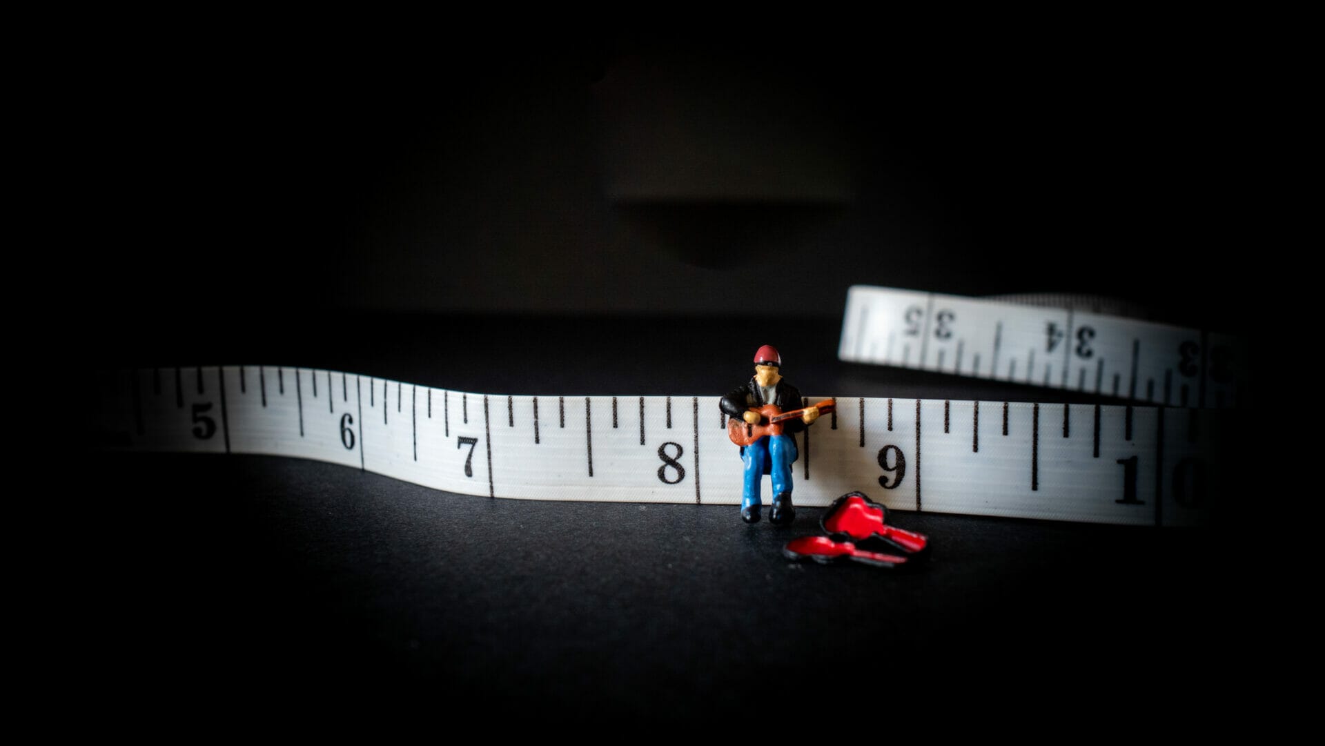 Creative photo showing a miniature model person playing a guitar on a tape measure.