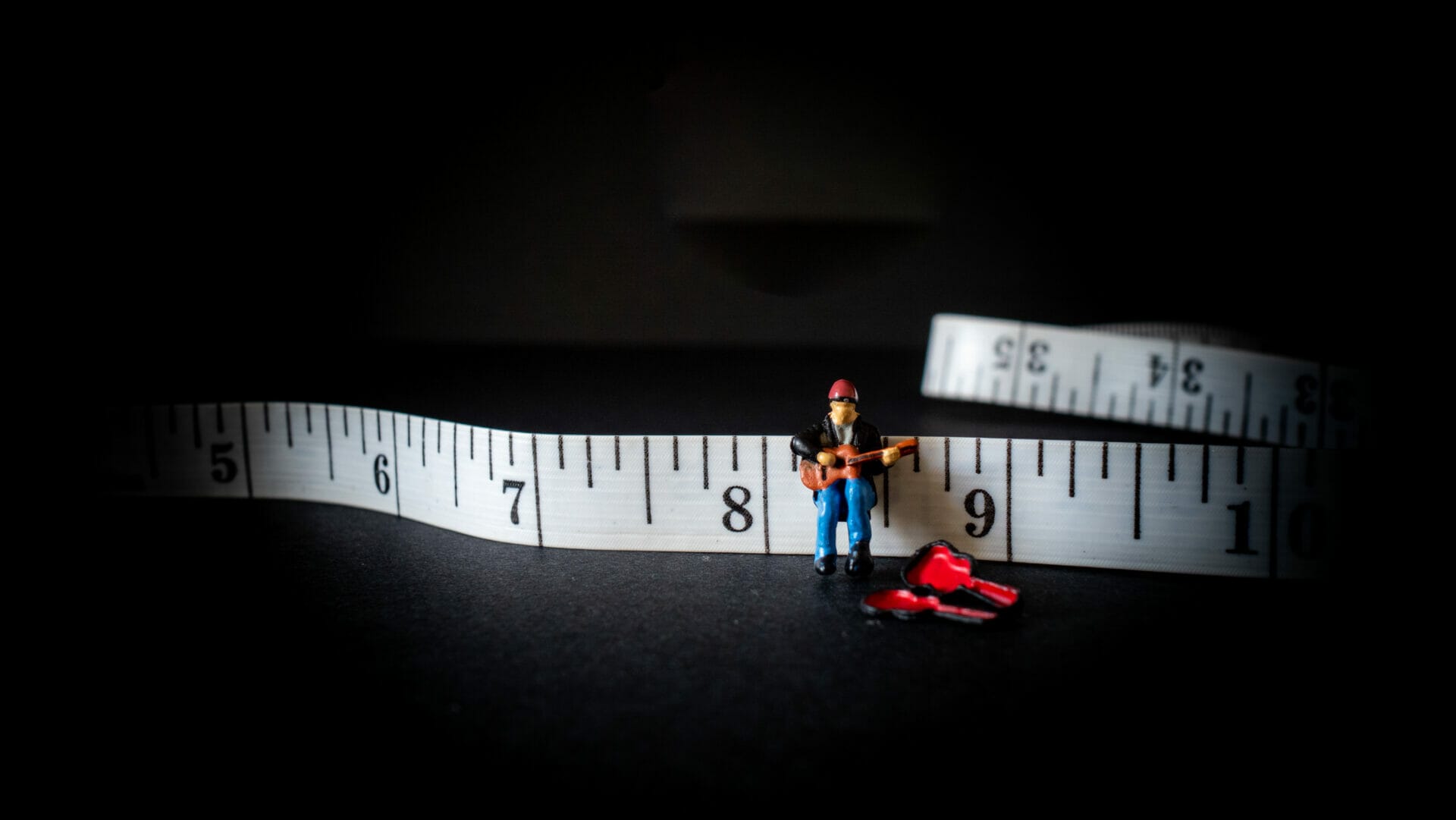Creative photo showing a miniature model person playing a guitar on a tape measure.