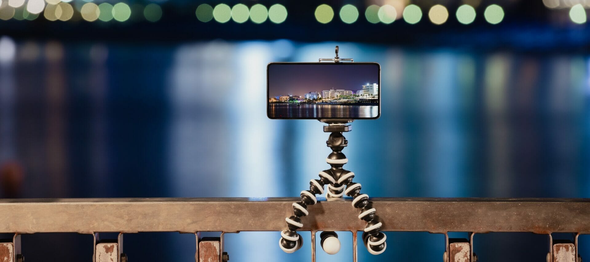 Two Minute Tuesdays - Table Top Tripods. Photo of a smart phone attached to a gorilla tripod twisted around a fence railing taking a photo at night