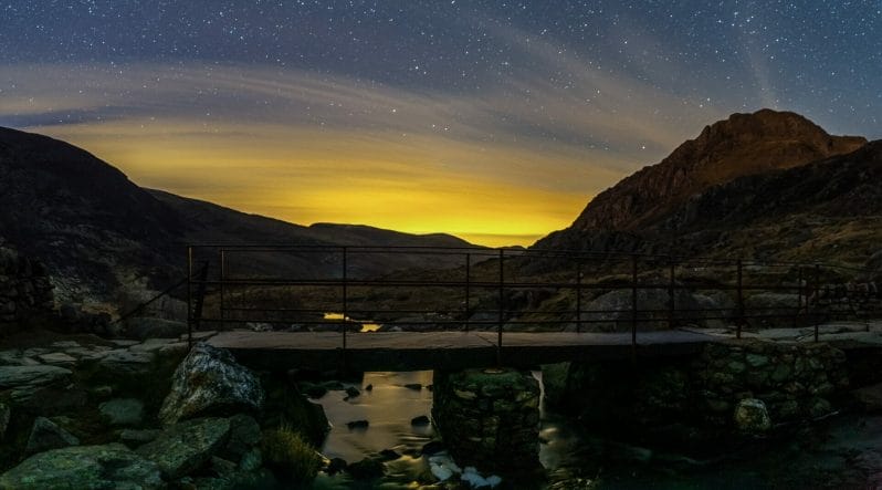 Photo of the night sky over a river and bridge surrounded by mountains - taken for the Astro & Night Photography Photographic workshop with Welshot Imaging